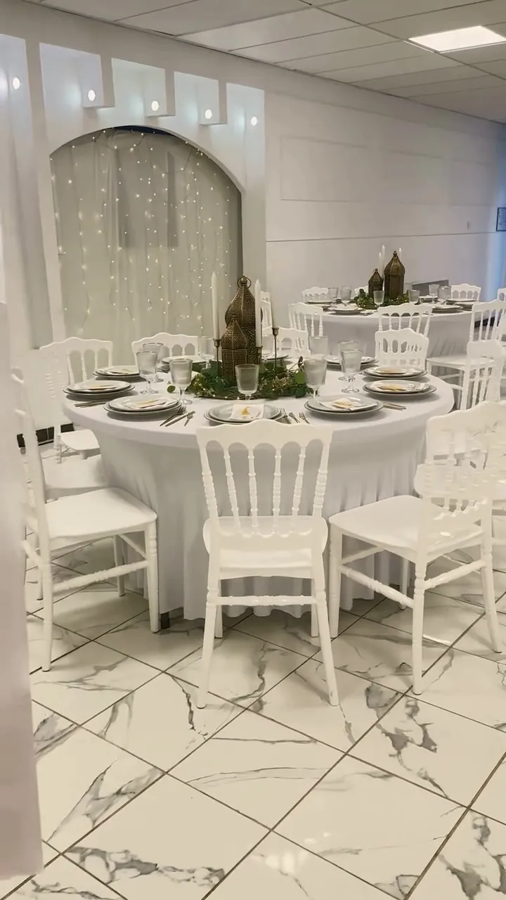 Tables rondes dressées avec lanternes, devant une arche ornée de rideaux lumineux