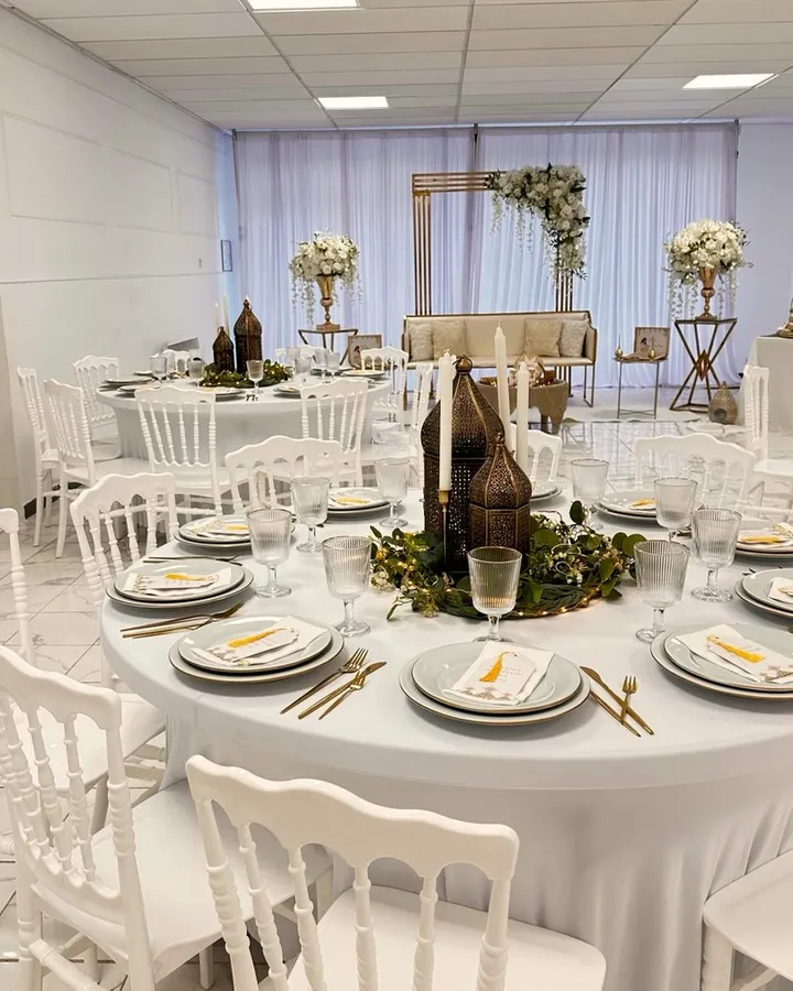 Table blanche décorée de lanternes dorées et de verdure, avec en fond une arche fleurie et un canapé